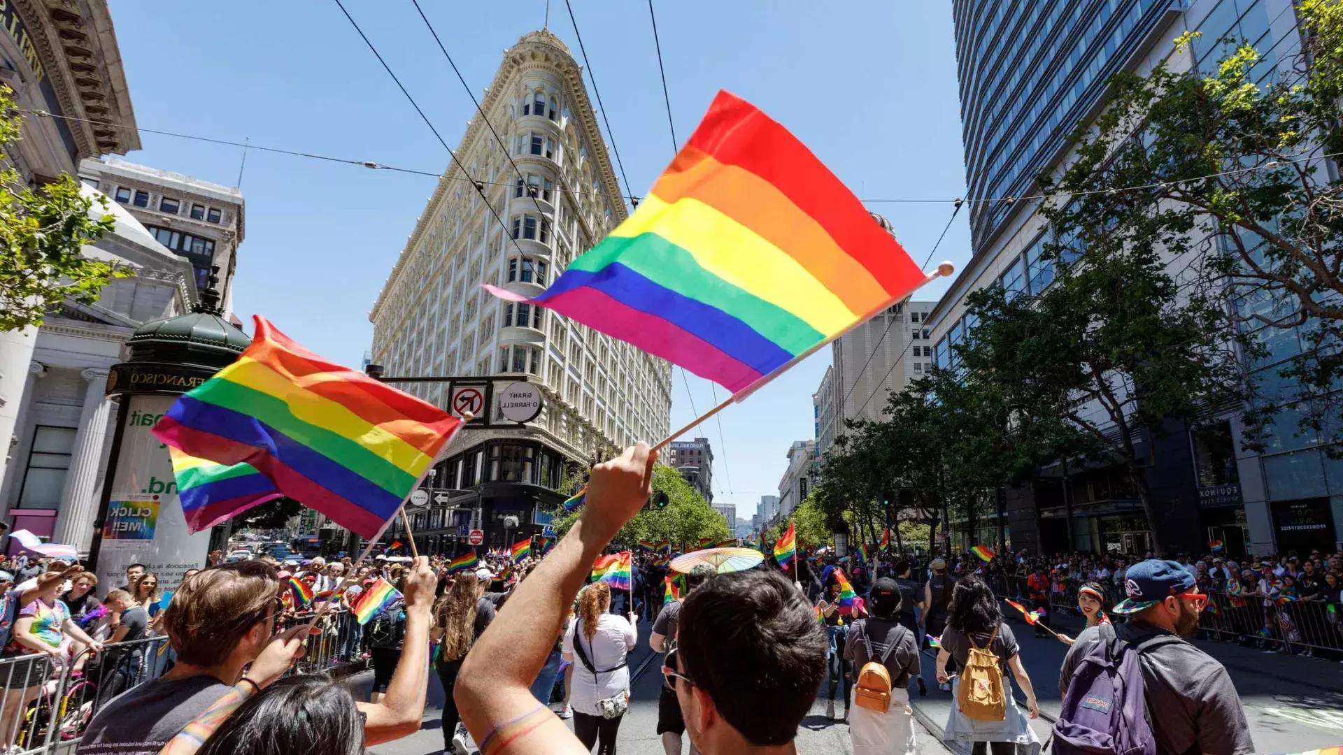 People walking in the San Francisco Pride parade wave rainbow flags.