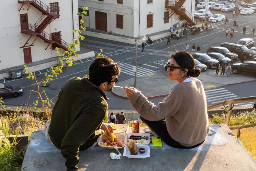 Un couple dîne en plein air au Fort Mason Center de San Francisco. La femme donne à son compagnon un avant-goût de la nourriture.