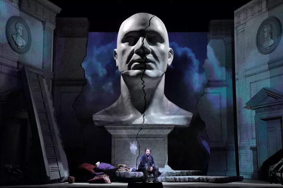 A giant bust of a man looms over two actors on stage in a production of Don Giovanni in San Francisco.