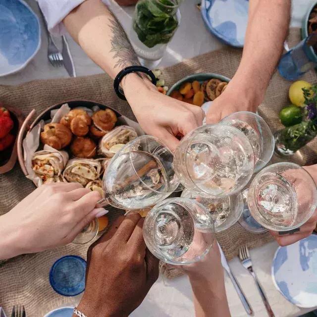 Fotografía cenital de un grupo de personas brindando vasos en una mesa de brunch.