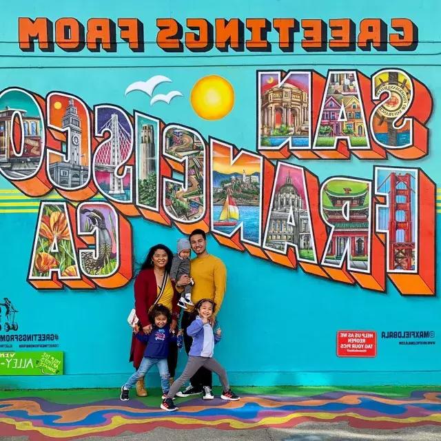 Una familia posando para una foto frente a un mural de San Francisco