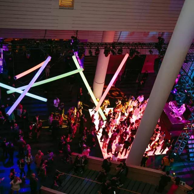 Image of people on a dance floor lit by rainbow neon lights hanging from ceiling
