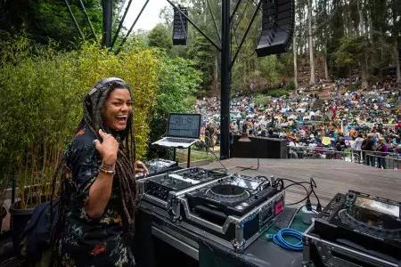 A woman DJing at the Stern Grove Festival looks over her shoulder and smiles into the camera.